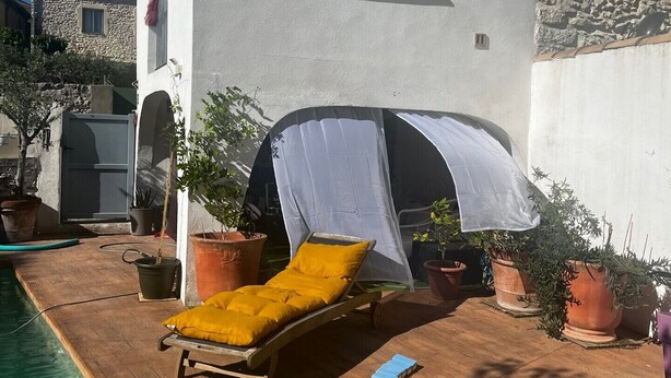A poolside area with a sun lounger, a covered seating area, and potted plants.