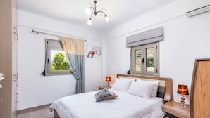 A bedroom with a bed, bedside lamps, a window with curtains, a wall-mounted air conditioner, and a wooden wardrobe.