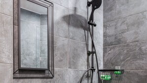 A modern bathroom with a stone sink, a handheld showerhead, and a mounted mirror.