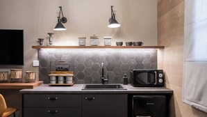 Una cocina compacta con microondas, hervidor y cafetera sobre la encimera, un lavabo y un armario debajo.
