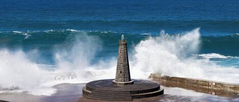 Un monumento de piedra junto al mar, con olas rompiendo cerca.