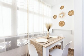 A dining area with a table set for two, white chairs, and a decorative vase.
