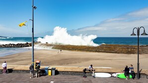 A beach with waves crashing onto the shore, a wooden walkway, and people near the water.