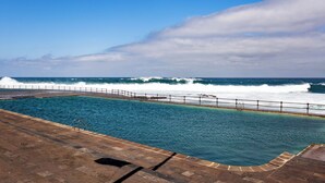 A swimming pool with a view of the ocean and waves crashing onto the shore.