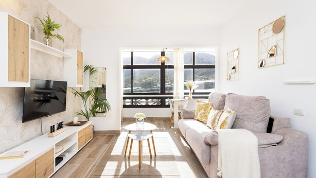 A modern living room with a flat-screen TV, a sofa, a coffee table, and a large window offering a scenic view.