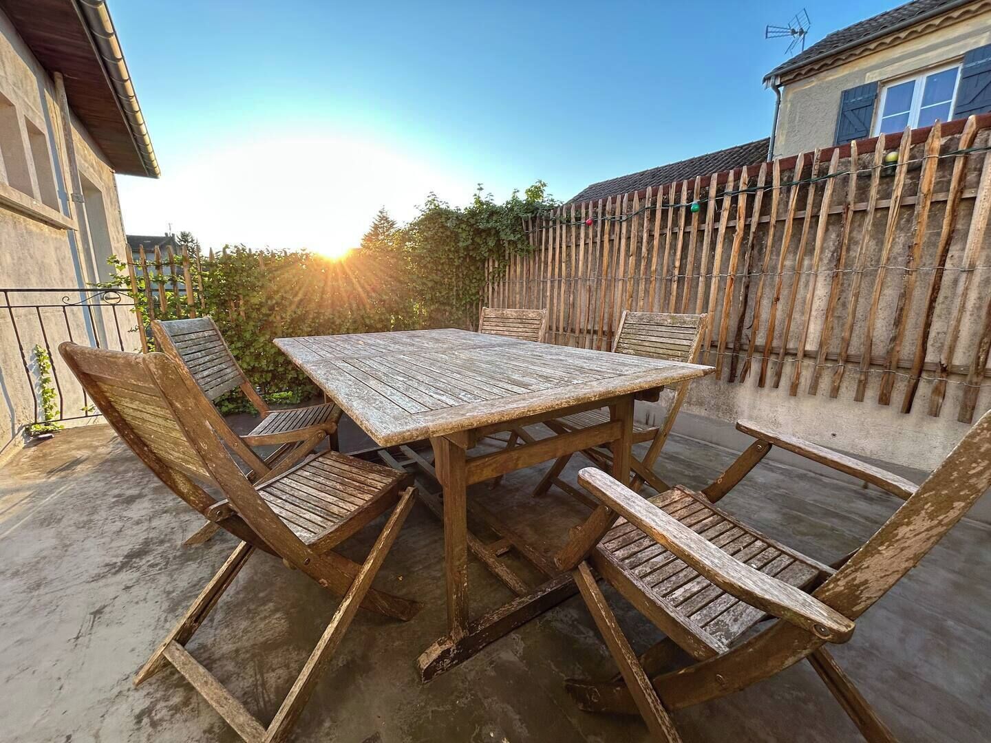 A wooden patio table with four chairs, surrounded by a wooden fence and a house in the background.