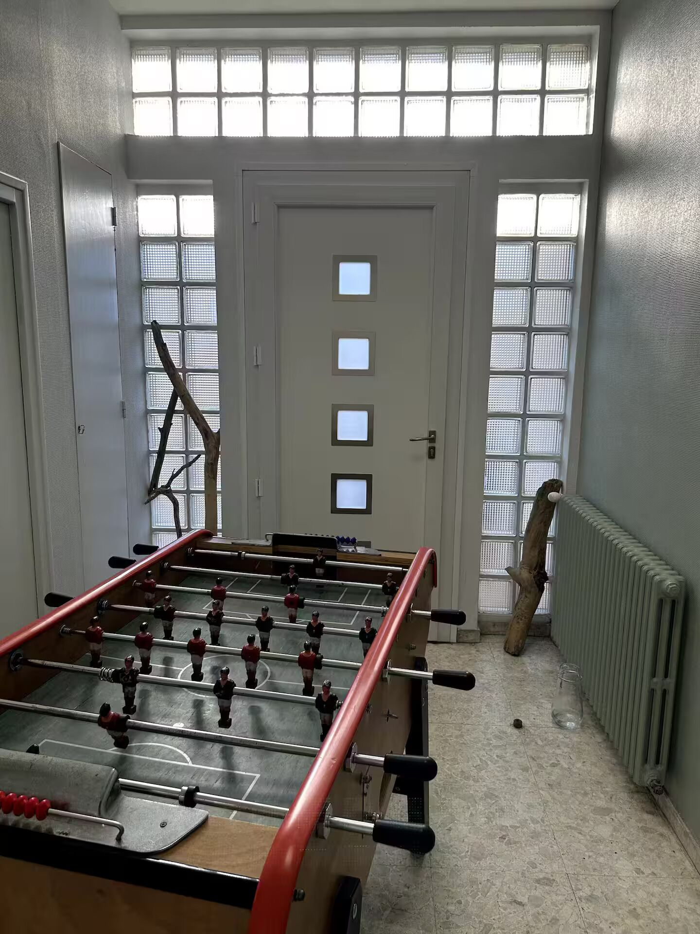 A room with a foosball table, a ladder leaning against the wall, and a radiator.