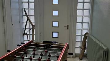 A room with a foosball table, a ladder leaning against the wall, and a radiator.