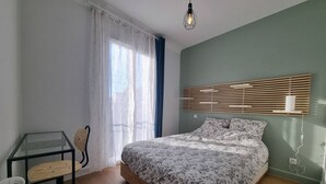 A bedroom with a bed, a desk, a chair, a window with curtains, and a hanging light fixture. - Les Cognassiers (Agen)