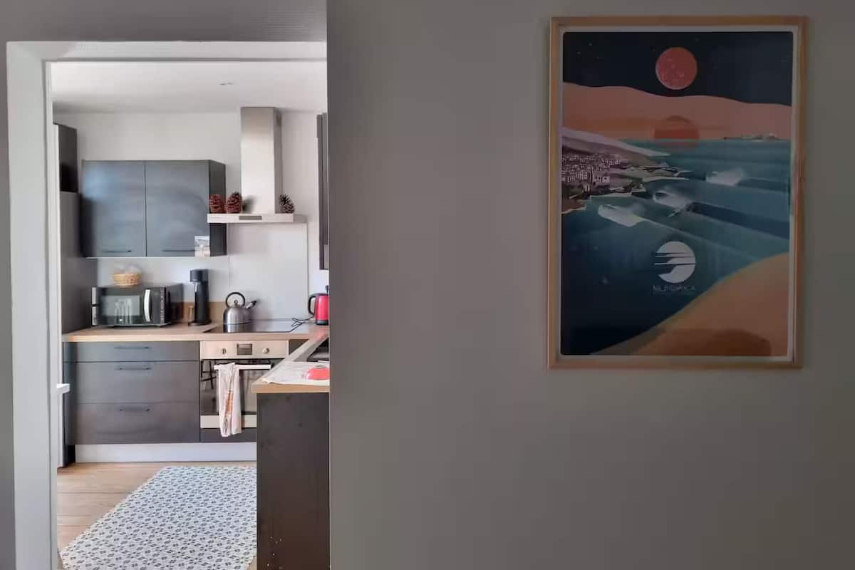 A modern kitchen with grey cabinets, a wooden countertop, and a red kettle.