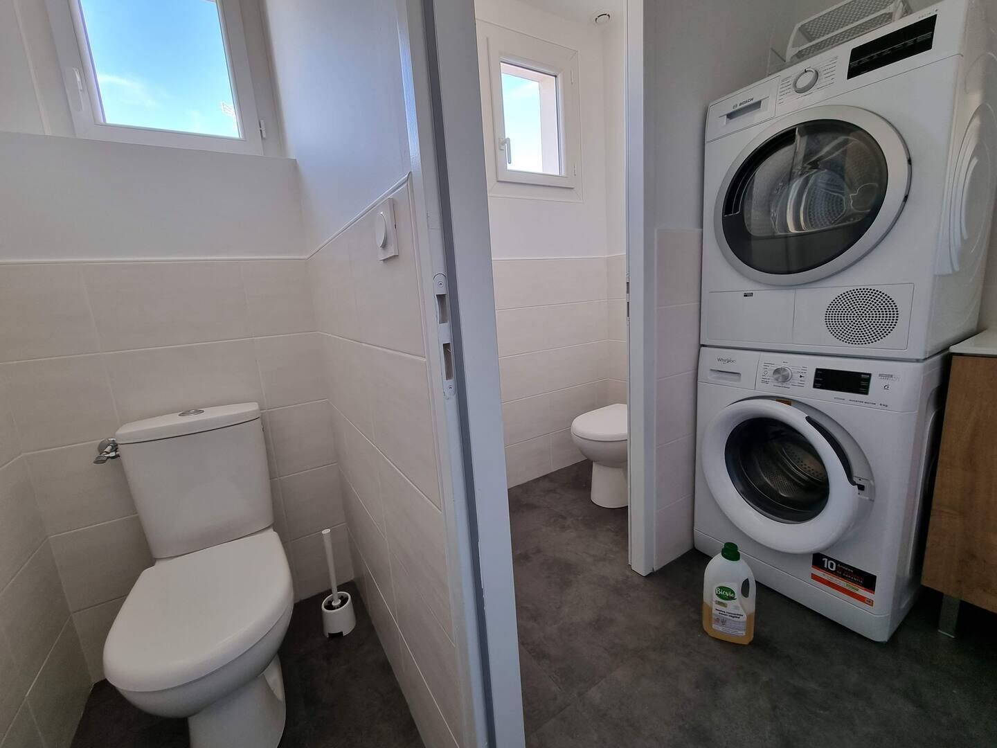 Ein kleines Badezimmer mit Toilette, Waschmaschine und Fenster.