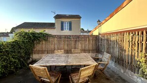 A wooden table with chairs in a courtyard, surrounded by a wooden fence and a yellow wall. - Les Cognassiers (Agen)