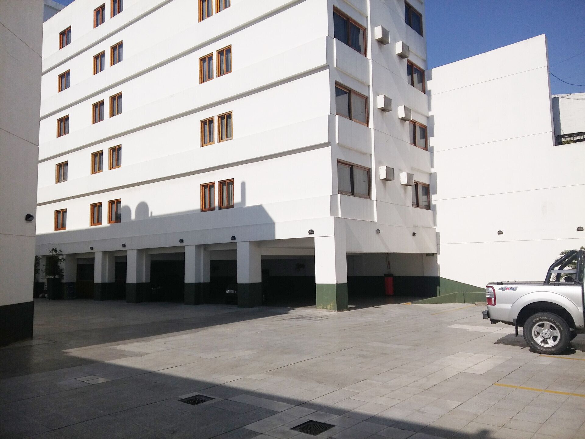 A multi-story building with a white facade, multiple windows, and a parking area with a white pickup truck.