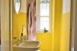 A bathroom with a yellow wall, a sink, a mirror, and a window with a curtain. - Rustico nel parco - Two Bedroom Apartment, Sleeps 4 (Piani Resinelli II)