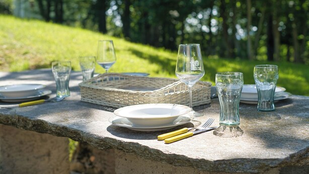 Mesa de piedra al aire libre con platos, vasos y cubiertos.