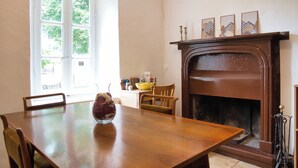 Un comedor con una mesa de madera, sillas, un jarrón de flores, chimenea y ventana con vistas a árboles.