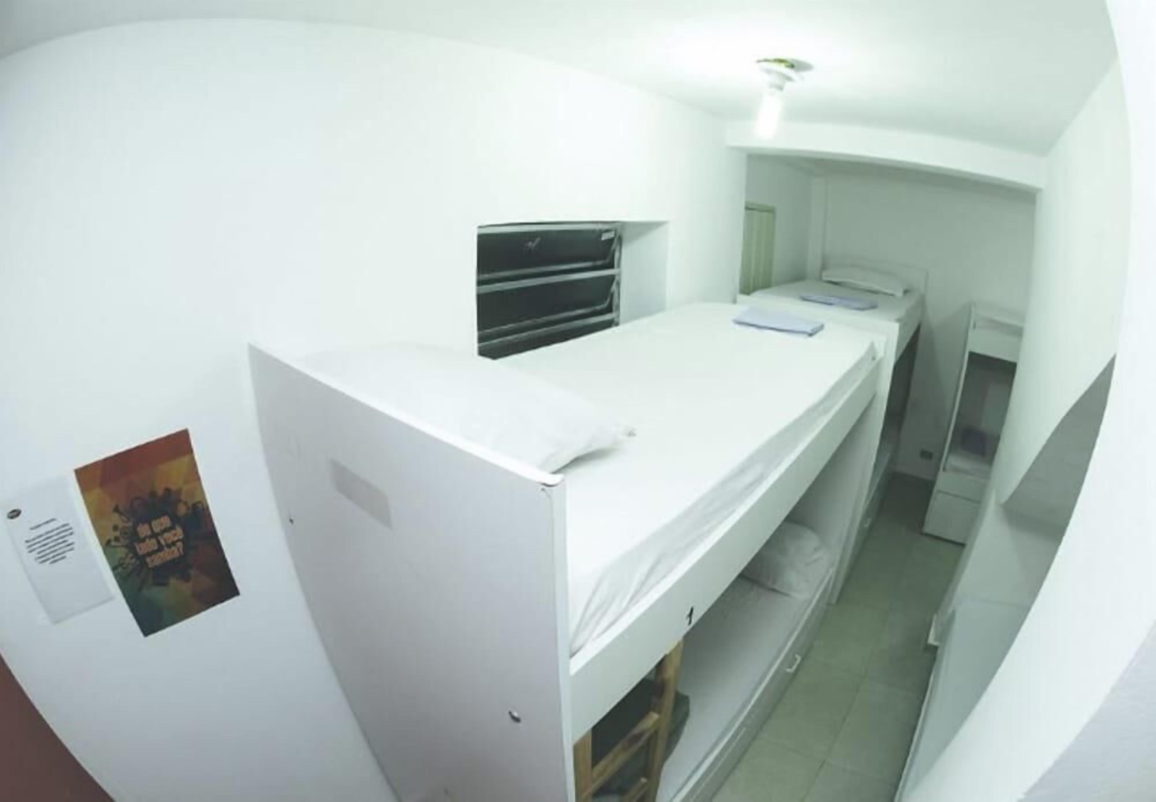 A narrow, white-walled room with a bunk bed, a small desk, and a window.