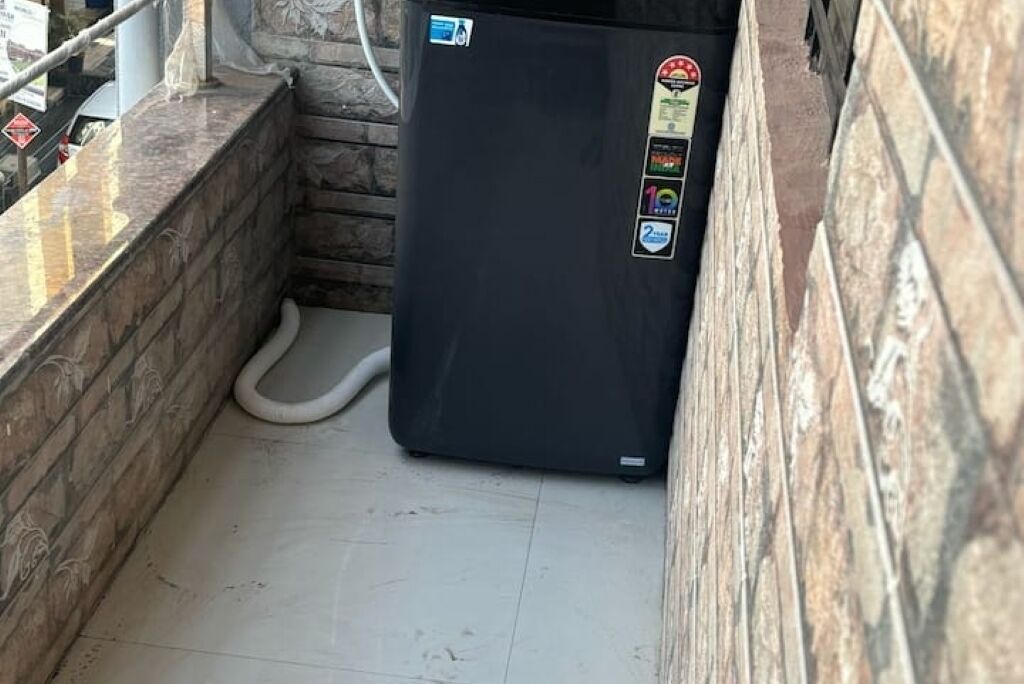 A compact, black refrigerator with a water dispenser, located in a narrow space with tiled flooring and a stone wall.