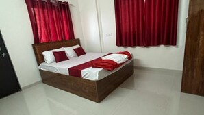 A neatly made bed with a wooden headboard, red curtains, and a white tiled floor. - 1BHK Comfy Stay 202 (Pune)