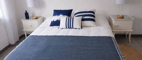 A bed with a blue and white bedspread, two bedside tables with lamps, and a woven rug on the floor.