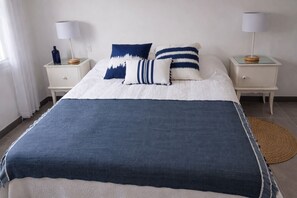A bed with a blue and white bedspread, two bedside tables with lamps, and a woven rug on the floor.