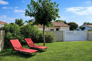 A backyard with two red lounge chairs, a tree, and a white fence.