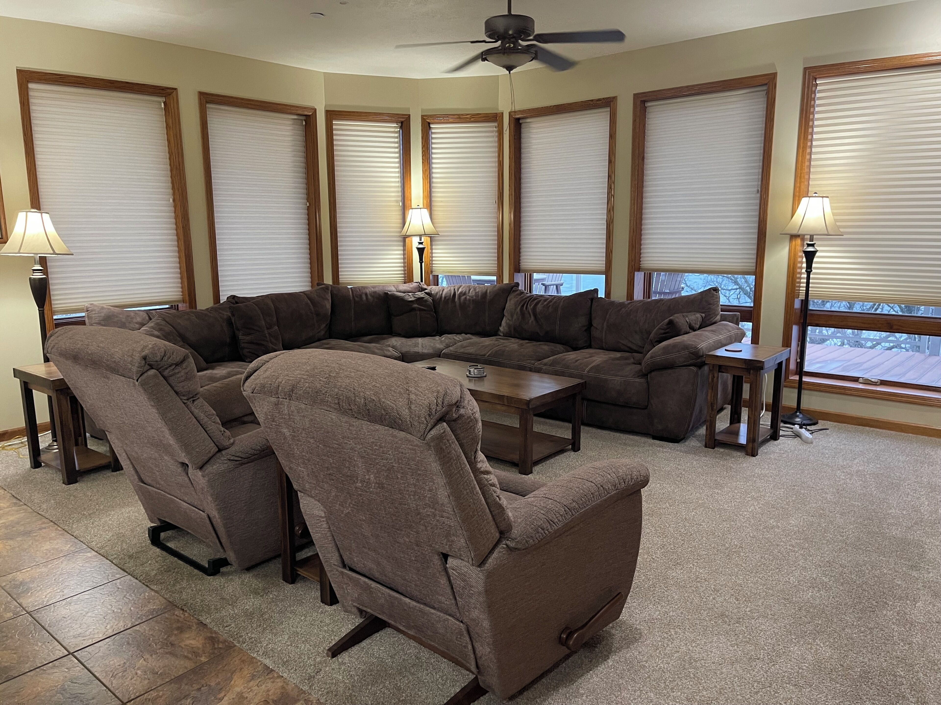 A sectional sofa with a small table, two floor lamps, and large windows with blinds.