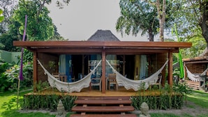 A wooden structure with a thatched roof, a hammock, and a statue in front. - Legian Villa Hotel (Porto Seguro)
