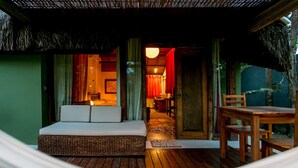 A cozy outdoor seating area with a thatched roof, a wooden table, and a cushioned bench. - Legian Villa Hotel (Porto Seguro)