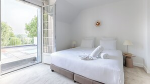 Quarto com uma cama grande, uma porta de vidro deslizante para uma varanda e uma pequena mesa de cabeceira com abajur.