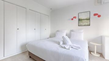 Een keurig opgemaakt slaapkamer met een groot bed, een garderobe, een klein tafeltje en een wandlamp.