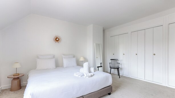 Quarto com cama grande, mesa de cabeceira, cadeira e guarda-roupa.
