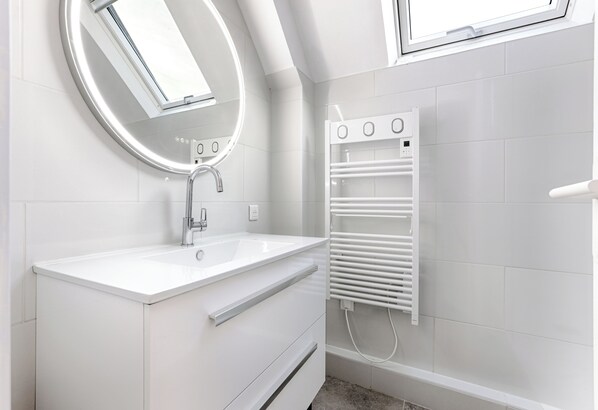 A modern bathroom with a white sink, a round mirror, and a built-in heater.