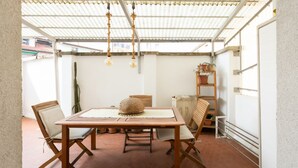 Um pátio ao ar livre com mesa e cadeiras de madeira, luminária pendente e um cacto ao fundo.