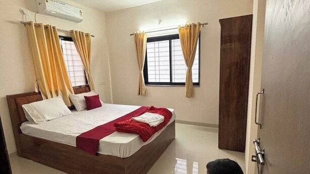 Un dormitorio con una cama de madera, paredes color beige y dos ventanas con cortinas.
