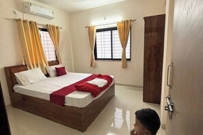 A bedroom with a wooden bed, beige walls, and two windows with curtains. - 1 bhk comfy stay 201 (Pune)