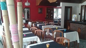 A restaurant with multiple tables and chairs, a red wall, and a brick counter. - Hotel Compostela (Necochea)