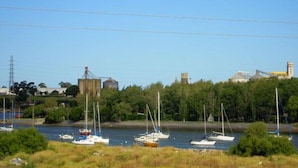 A marina with several sailboats docked, surrounded by greenery and industrial buildings in the background. - Hotel Compostela (Necochea)