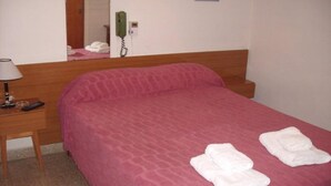 A hotel room with a single bed, a bedside table with a lamp, a telephone, and a mirror. - Hotel Compostela (Necochea)