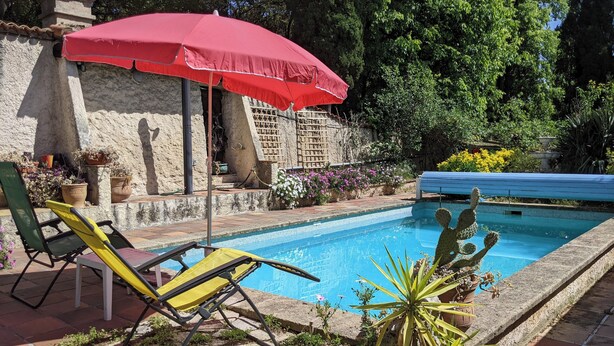 A pool area with a red umbrella, a yellow chair, and various plants. - Villa with swimming pool and garden. (Marseille)