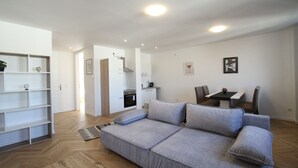 A modern living room with a grey sofa, a bookshelf, and a dining area with chairs and a table. - Margot (Vienna)