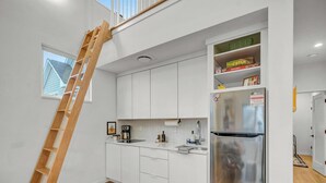 A modern kitchen with white cabinets, a stainless steel refrigerator, and a wooden ladder.
