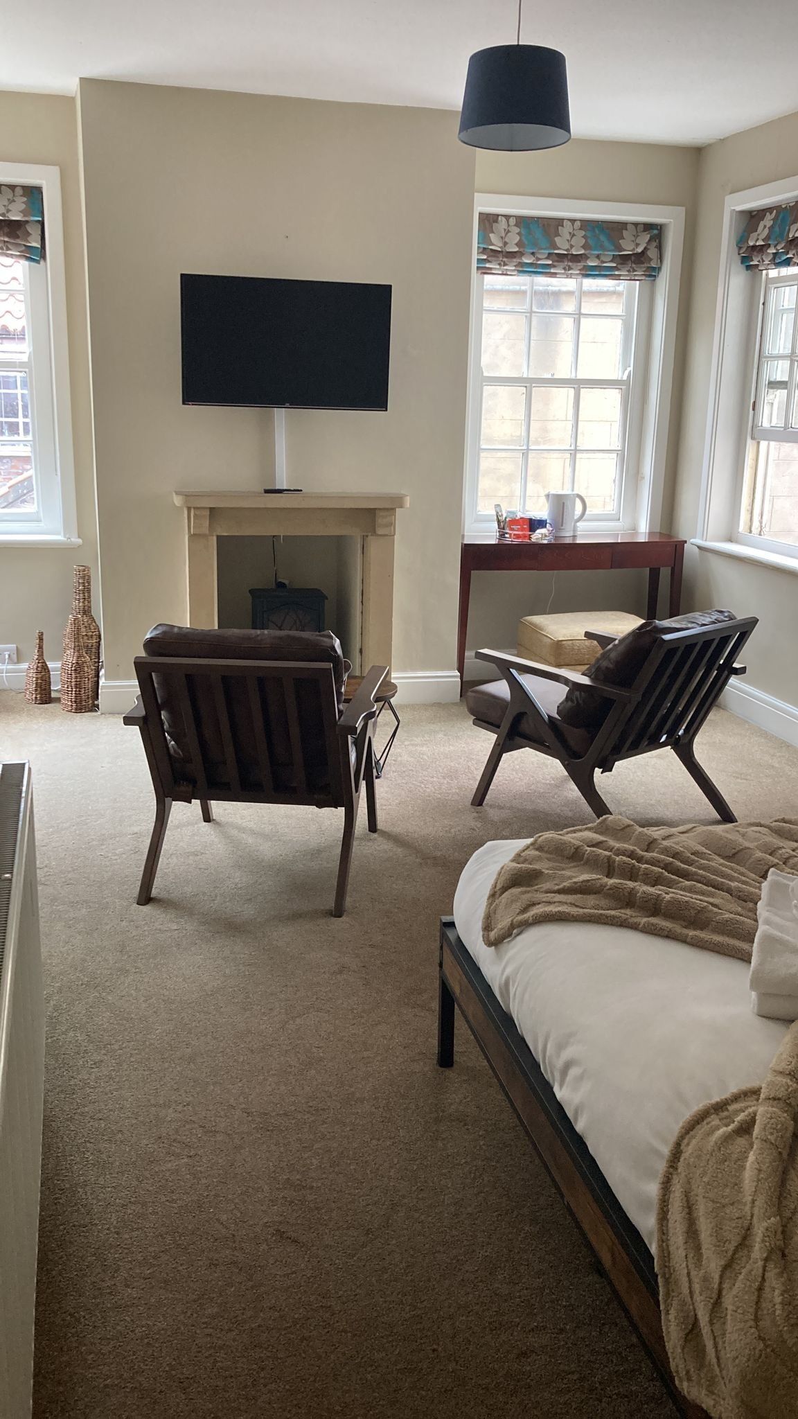 Une chambre à coucher comprenant un lit, deux fauteuils, une cheminée, un téléviseur et de grandes fenêtres.