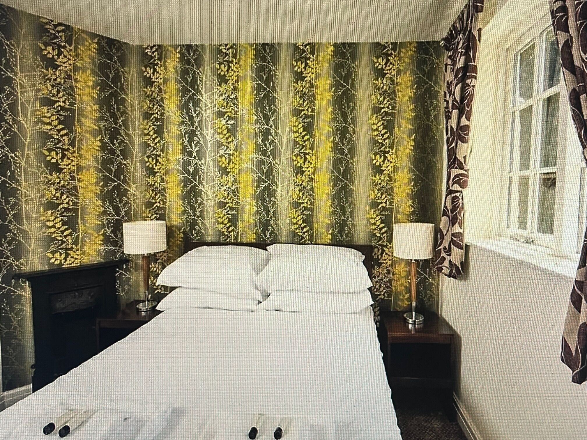 Una habitación de hotel con una cama grande, dos mesitas de noche y una ventana con cortinas.