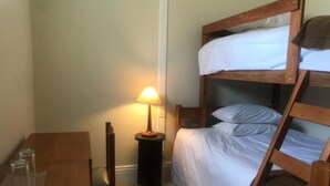 A bunk bed with white bedding, a small wooden table with two glasses, a chair, and a bedside lamp. - Hotel Plaza Central (Arequipa)