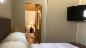 A hotel room with a bed, a TV mounted on the wall, and a door leading to a hallway with a lamp. - Hotel Plaza Central (Arequipa)