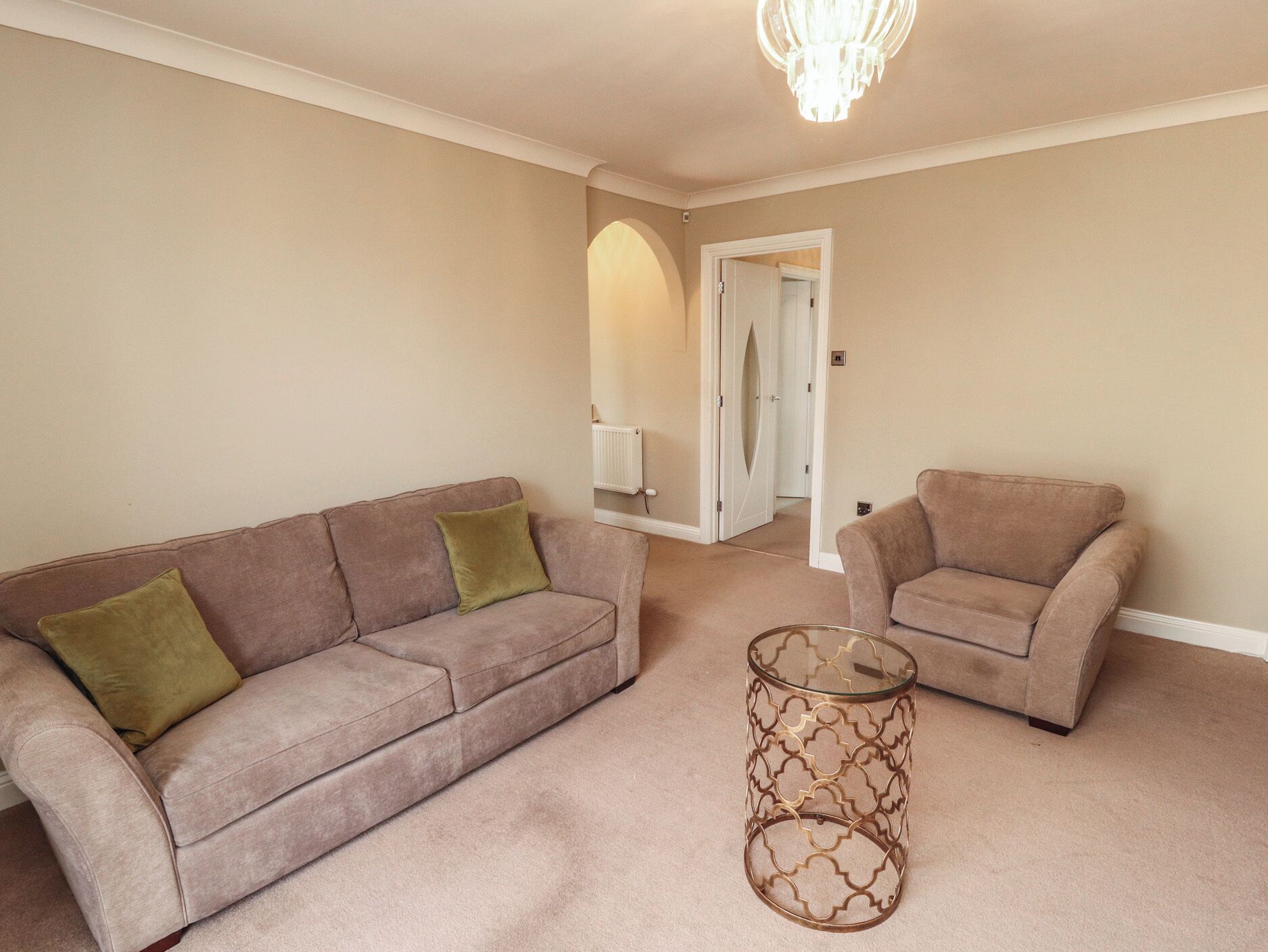 A living room with a beige sofa, a matching armchair, and a glass coffee table.