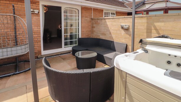 A covered patio area with a hot tub, wicker furniture, and a glass door leading to a garage. - 3 Hawk Place (Whitehaven)