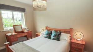 A bedroom with a large bed, wooden nightstands, a dresser, a vanity with a mirror, and a chandelier. - 3 Hawk Place (Whitehaven)