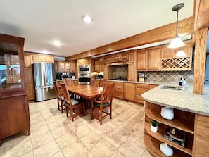 Una cocina con armarios de madera, una mesa de comedor con sillas, un refrigerador, un horno y un lavaplatos.